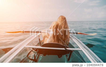 Woman in kayak back view. Happy young woman with long hair floating in transparent kayak on the crystal clear sea. Summer holiday vacation and cheerful female people relaxing having fun on the boat Woman in kayak back view. Happy young woman with long hair floating in transparent kayak on the crystal clear sea. Summer holiday vacation and cheerful female people relaxing having fun on the boat 104094478