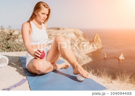 Woman sea pilates. Sporty happy middle aged woman practicing fitness on yoga mat with balls and roller near sea, smiling active female outside, enjoying healthy lifestyle, harmony and meditation. 104094488
