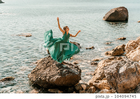 Woman green dress sea. Female dancer in a long mint dress posing on a beach with rocks on sunny day. Girl on the nature on blue sky background. Woman green dress sea. Female dancer in a long mint dress posing on a beach with rocks on sunny day. Girl on the nature on blue sky background. 104094745