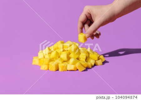 Pineapple pieces on a purple background. Woman hand taking pineapple 104094874