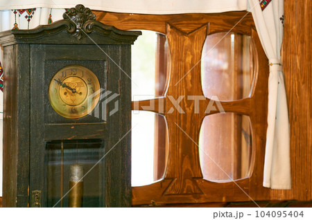 Vintage clock in a black wooden case by the window with a wooden frame Vintage clock in a black wooden case by the window with a wooden frame 104095404