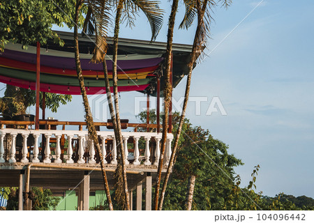 Terrace architecture with palm trees in front of fenced restaurant balcony and decorated roof at Costa Rica Terrace architecture with palm trees in front of fenced restaurant balcony and decorated roof at Costa Rica 104096442