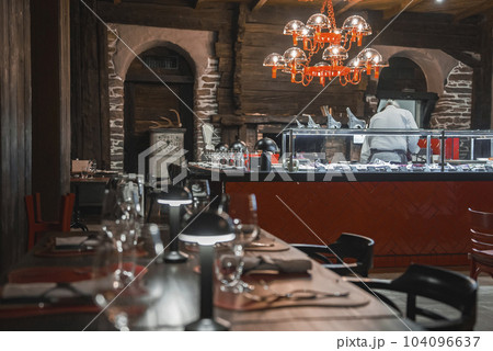 Illuminated chandelier hanging over chef working at food counter and place setting with lights on dining table in luxurious restaurant at hotel, luxury travel concept Illuminated chandelier hanging over chef working at food counter and place setting with lights on dining table in luxurious restaurant at hotel, luxury travel concept 104096637