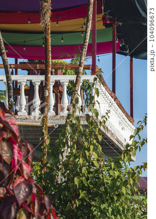 Terrace architecture with fenced restaurant balcony and decorated colorful roof. Trees and plant in the foreground at Costa Rica Terrace architecture with fenced restaurant balcony and decorated colorful roof. Trees and plant in the foreground at Costa Rica 104096673