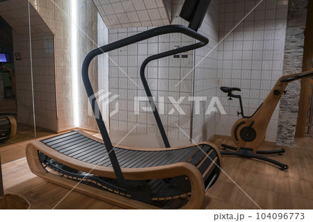 Wooden treadmill with cycle placed on hardwood floor by tiled wall in empty gym at luxury hotel, luxury travel and fitness concept for tourists Wooden treadmill with cycle placed on hardwood floor by tiled wall in empty gym at luxury hotel, luxury travel and fitness concept for tourists 104096773