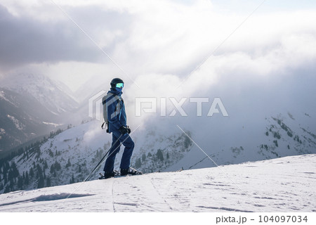 Tourist with ski poles skiing on snow covered mountain with cloudy sky in background during winter vacation, winter holiday travel concept 104097034