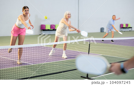 Two athletic women of different ages are playing a game of pickleball on a court inside sports facility 104097245