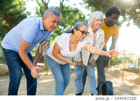 Cheerful males and females playing petanque in park on holidays Cheerful males and females playing petanque in park on holidays 104097280