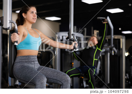 Girl performing butterfly exercise for chest in pec deck machine 104097298