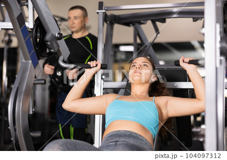 Fit young woman working out at shoulder press machine in gym 104097312