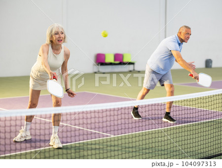 Athletic seniors playing pickleball on court indoors 104097313