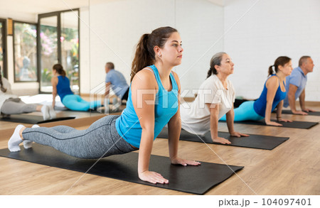 Class of male and women of different ages in active wear doing cobra exercise exercise during Pilates training together in gym Class of male and women of different ages in active wear doing cobra exercise exercise during Pilates training together in gym 104097401