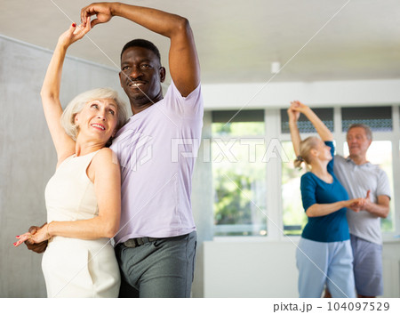 Mature men and women practicing Ballroom dances in training room Mature men and women practicing Ballroom dances in training room 104097529