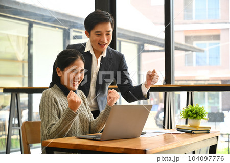 Happy businesspeople looking at laptop screen excited by good news online, celebrating success raising hands up 104097776