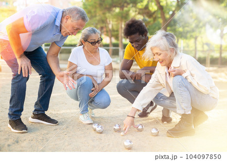 Positive mature diverse percioners comparing the distance of pumped balls after petangue at the sunny afternoon outdoors 104097850