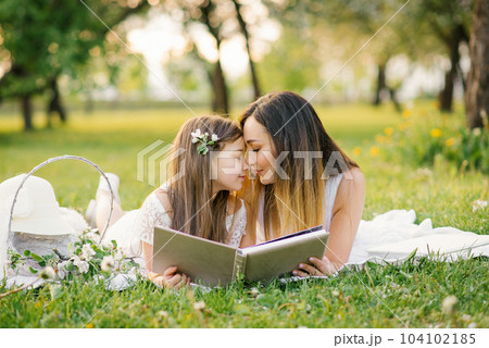 Happy family mom and daughter are watching an album with photos in the summer in the park or in the garden 104102185