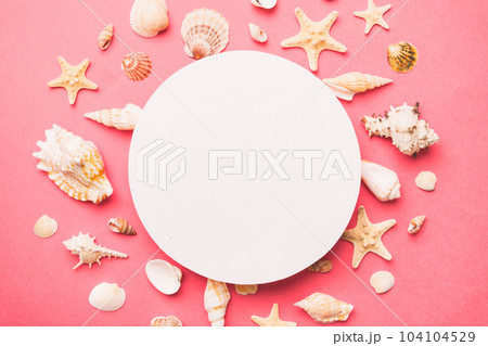 Summer time concept with blank greeting card and blank white paper on colored background. Seashells from ocean shore in the shape of frame separated with space for text top view 104104529