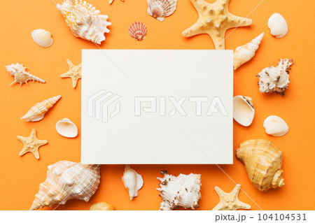 Summer time concept with blank greeting card and blank white paper on colored background. Seashells from ocean shore in the shape of frame separated with space for text top view Summer time concept with blank greeting card and blank white paper on colored background. Seashells from ocean shore in the shape of frame separated with space for text top view 104104531
