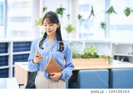 オフィスでスマホを操作するビジネスカジュアルの若い女性 104106103