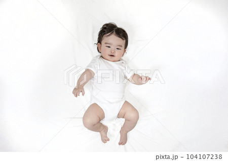 白シーツのベットに仰向け状態でカメラ目線の乳幼児の全身姿 白シーツのベットに仰向け状態でカメラ目線の乳幼児の全身姿 104107238