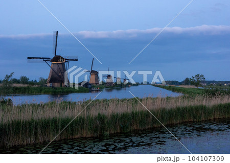 Beautiful wooden windmills at sunset in the Dutch village of Kinderdijk. Windmills run on the wind. The beautiful Dutch canals are filled with water. Beautiful sunset. Beautiful wooden windmills at sunset in the Dutch village of Kinderdijk. Windmills run on the wind. The beautiful Dutch canals are filled with water. Beautiful sunset. 104107309