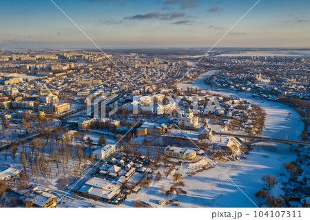 Nice top view of the winter city. Houses and buildings in the snow. Bridge over river. Orthodox churches and a Catholic cathedral. The river is covered with ice. Nice top view of the winter city. Houses and buildings in the snow. Bridge over river. Orthodox churches and a Catholic cathedral. The river is covered with ice. 104107311