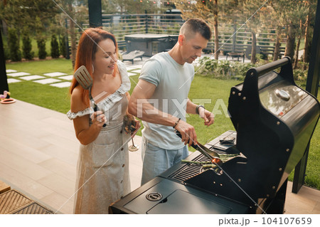A married couple cooks grilled meat together on their terrace A married couple cooks grilled meat together on their terrace 104107659