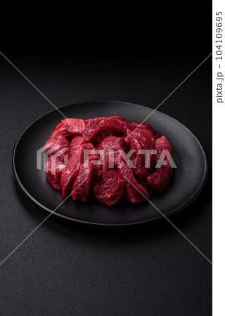 Juicy raw beef with spices, salt and herbs on a dark concrete background 104109695