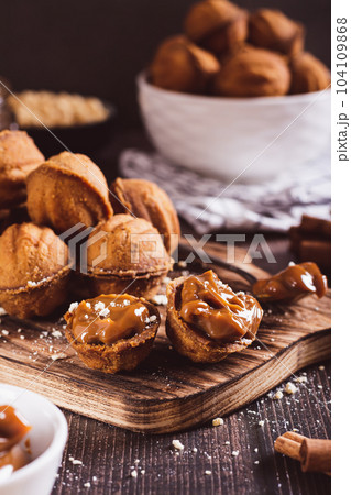 Homemade walnut shaped cookies filled with boiled condensed milk on a board vertical view Homemade walnut shaped cookies filled with boiled condensed milk on a board vertical view 104109868