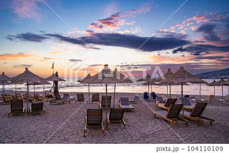 Sunshade beach umbrellas with sunset sky and sea background. Sarande, Albania  104110109