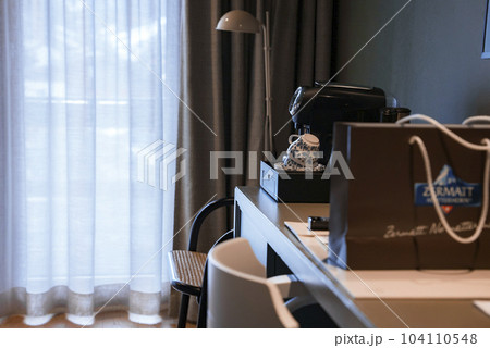 Coffee machine with cups and shopping bag on table with chairs inside bedroom at luxurious alpine hotel, hotel interior design concept 104110548
