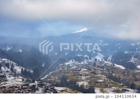 Aerial view of houses and trees on landscape in Grindelwald village with majestic mountains and cloudy sky in background at Jungfrau, Switzerland, winter holiday concept 104110634