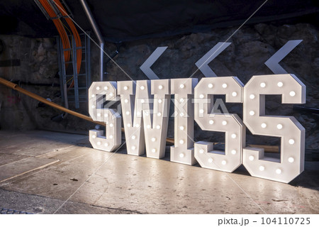 Illuminated white structure of swiss text on floor and arrow signs on rocky wall at Jungfrau railway station in mountain tunnel inside Bernese Alps, Switzerland, winter holiday travel concept Illuminated white structure of swiss text on floor and arrow signs on rocky wall at Jungfrau railway station in mountain tunnel inside Bernese Alps, Switzerland, winter holiday travel concept 104110725