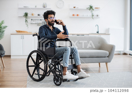 Adult in wheelchair talking on cell phone in studio flat Adult in wheelchair talking on cell phone in studio flat 104112098