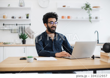 Freelancer operating laptop while sitting at desk in kitchen Freelancer operating laptop while sitting at desk in kitchen 104112937