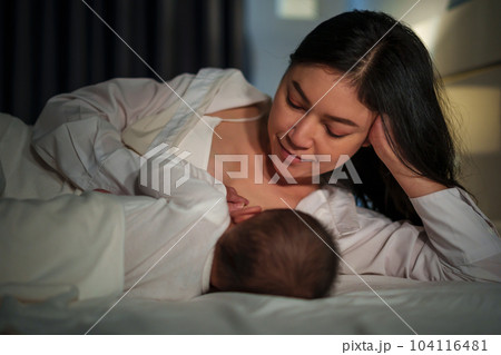 mother is breastfeeding a infant baby while lying and sleeping on bed at night mother is breastfeeding a infant baby while lying and sleeping on bed at night 104116481