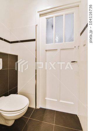 a bathroom with black and white tile flooring on the walls, door to the left and toilet in the middle a bathroom with black and white tile flooring on the walls, door to the left and toilet in the middle 104116736