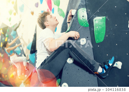 Teen guy practicing rock climbing on climbing wall Teen guy practicing rock climbing on climbing wall 104116838