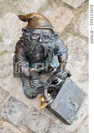 Dwarf with a padlock near bridge. Small bronze figures of gnomes on the streets of Wroclaw. Europe Miniature bronze figure of a gnome. Symbol of Wroclaw 104121616