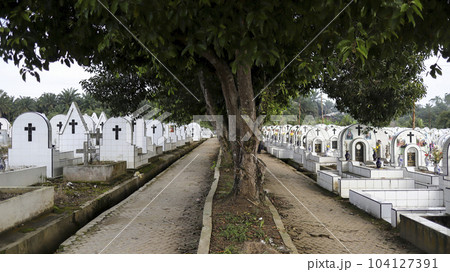 The public cemetery pathway contains identical white ceramic graves at the left and right. The public cemetery pathway contains identical white ceramic graves at the left and right. 104127391