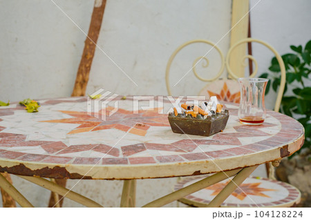 Ashtray with cigarette butts and a glass of tea, smoking on the streets of cities or in cafes, the choice and power of traditions, health care, the dangers of smoking 104128224