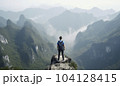 Hiker with backpack on a rocky ledge enjoys the view down the valley to a lake - AI content 104128415
