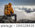 Hiker with mountaineering gear on a ledge above the clouds enjoys the view - AI content 104128416