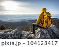 Hiker with mountaineering gear sitting on a ledge enjoys the view down thew valley - AI content 104128417