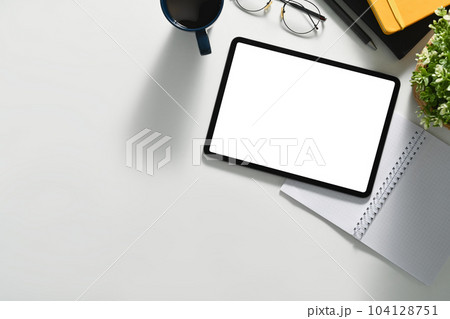 Top view of modern workplace with digital tablet, coffee cup, glasses and notepad on white working desk 104128751