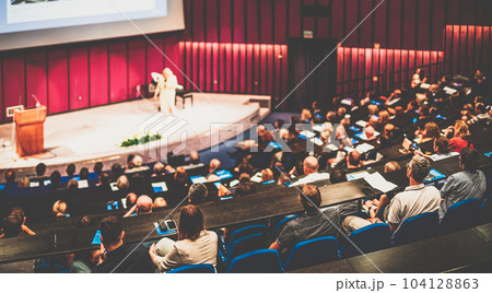 Business and entrepreneurship symposium. Female speaker giving a talk at business meeting. Audience in conference hall. Rear view of unrecognized participant in audience. Business and entrepreneurship symposium. Female speaker giving a talk at business meeting. Audience in conference hall. Rear view of unrecognized participant in audience. 104128863