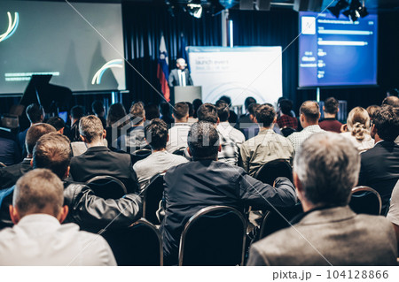 Speaker giving a talk in conference hall at business event. Rear view of unrecognizable people in audience at the conference hall. Business and entrepreneurship concept 104128866