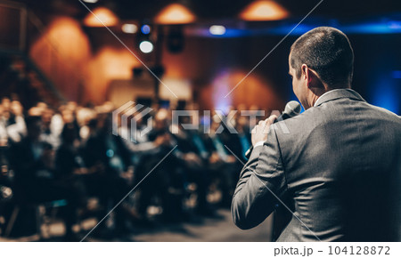 Speaker giving a talk on corporate business conference. Unrecognizable people in audience at conference hall. Business and Entrepreneurship event. Speaker giving a talk on corporate business conference. Unrecognizable people in audience at conference hall. Business and Entrepreneurship event. 104128872