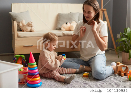 Mom and daughter playing together at a group lesson in the Montessori center, mommy and baby in casual clothes sitting on floor on carpet playing with colorful blocks. Mom and daughter playing together at a group lesson in the Montessori center, mommy and baby in casual clothes sitting on floor on carpet playing with colorful blocks. 104130982