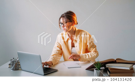 Online job. Laptop browsing. Network search. Concentrated woman freelancer working distance education using computer sitting at table against gray wall with copy space. Online job. Laptop browsing. Network search. Concentrated woman freelancer working distance education using computer sitting at table against gray wall with copy space. 104131420